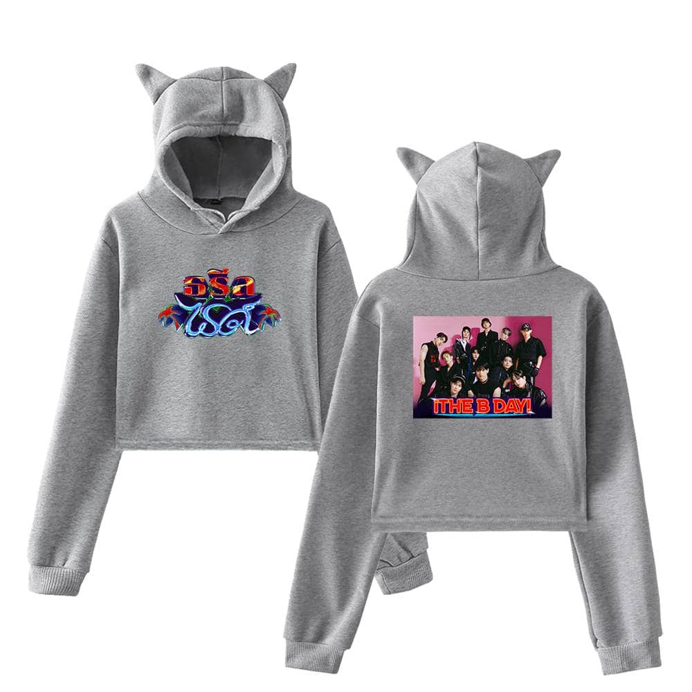Comfy gray hooded sweatshirt with playful cat ears, featuring colorful text and a vibrant K-pop group printed on the back suitable for fans of trendy streetwear and music merchandise.