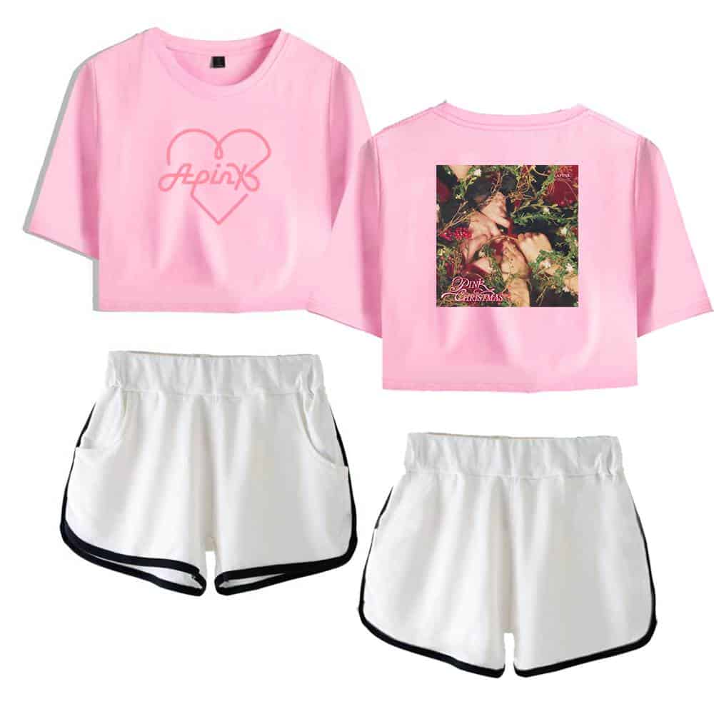 Pink cropped t-shirt with Heart and "Apink" logo, back print featuring a woman surrounded by flowers, paired with white sporty shorts with black trim. Perfect for casual or music event wear.