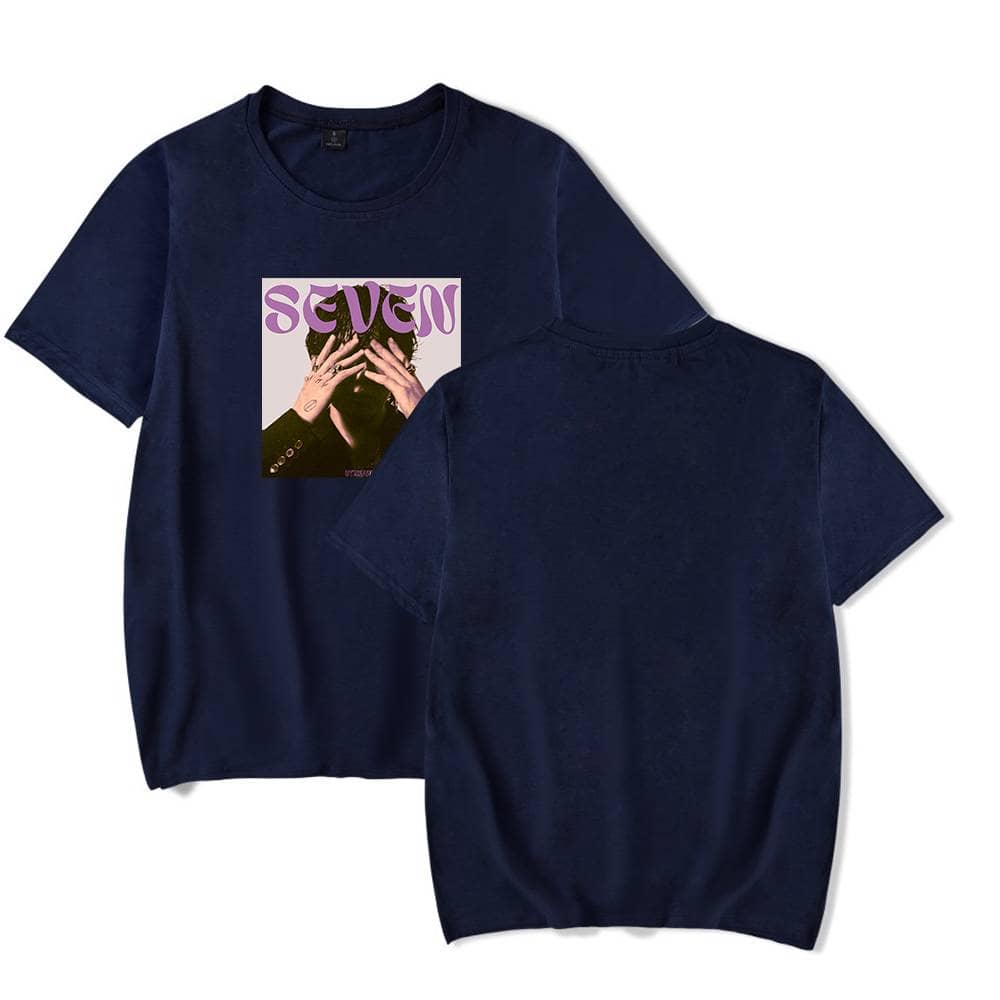 Silhouette of a navy blue t-shirt featuring a graphic print of a person with hands covering their face, and the word "Seven" in purple stylized text above. The back view shows a plain navy blue design.